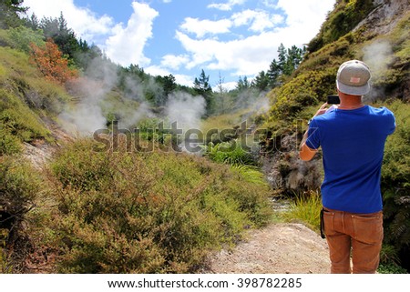 Man taking picture of hiking the trail and geothermal activity on the background, near Dragon's Mouth Geyser, Wairakei, New Zealand.