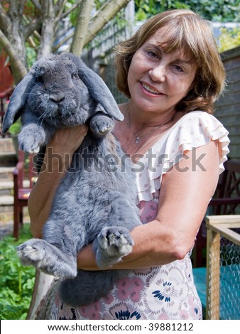 Smiling mature woman holding blue colored French Lop rabbit outdoors