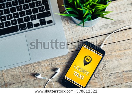 Locate Taxi message on a mobile phone screen.Office wooden desk with laptop computer and a plant.