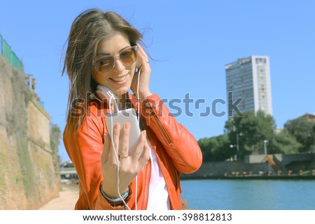 happy urban girl with smartphone and headphones enjoying streaming video, digital music on mobile connection - concept of teenagers freedom, music and modern lifestyle - faded custom color tones