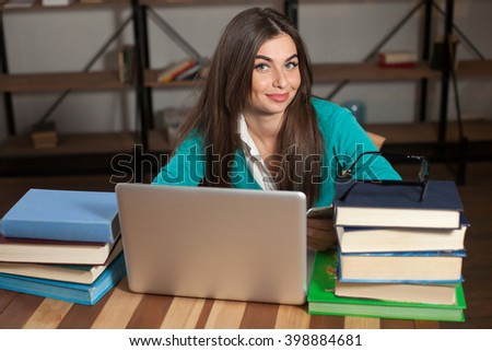 Beautiful woman is happy about her successful work with her grey laptop and books at the wood table