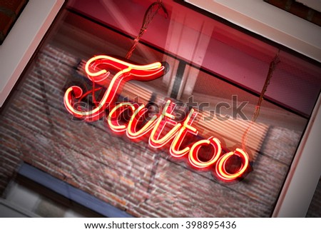 Tattoo sign, neon sign in a tattoo shop window. Red information sign, view from outside into a store. 