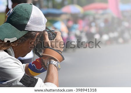 Photographer taking photo with professional digital camera outdoors, people shopping at market street in sunny day, blur background with bokeh