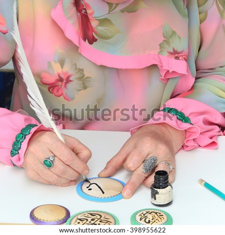 close-up of female hands artist in Tatar national costume, making Arabic calligraphy painting 