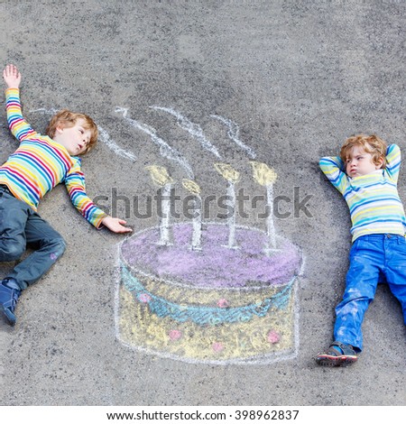 Two happy little kids having fun with big birthday cake picture drawing with colorful chalks. Creative leisure for children outdoors in summer. Kids blowing candles.