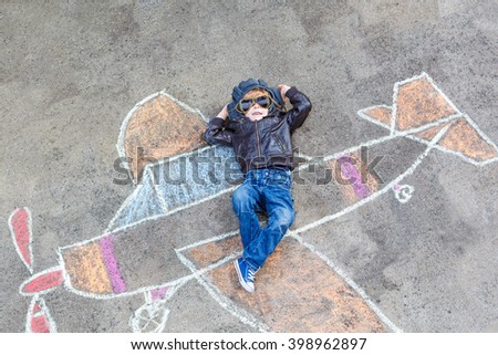 Funny little kid boy flying by a plane picture painting with colorful chalk. Creative leisure for children outdoors in summer. Child playing the little prince figure.