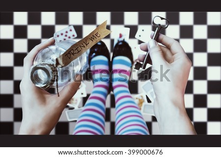 Alice in wonderland. Background. A key and a potion in hands against a  chess floor Royalty-Free Stock Photo #399000676