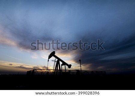 Cloudy sunset and silhouette of crude oil pump in the oil field.