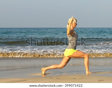 Slim 40s of age woman stretching, morning exercise, yoga posing on sand beach