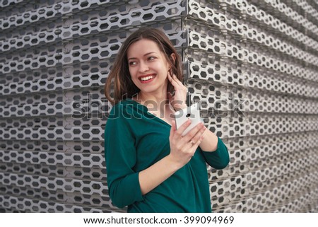 Young smiling female with  white smart-phone in hands on metal panel background