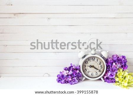 Background with white alarm clock and hydrangea flowers on white painted wooden planks. Place for text. 