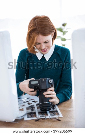 smiling hipster photographer looking at pictures on her camera, sitting at her desk