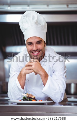 Chef leaning on the counter with a dish in a commercial kitchen