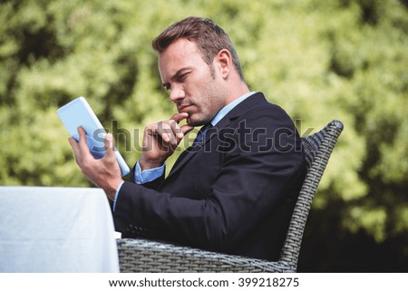 Thoughtful businessman using tablet sitting outside a restaurant