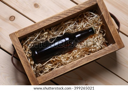 Bottle of beer in a wooden crate with wood shavings on a bright wooden surface Royalty-Free Stock Photo #399265021