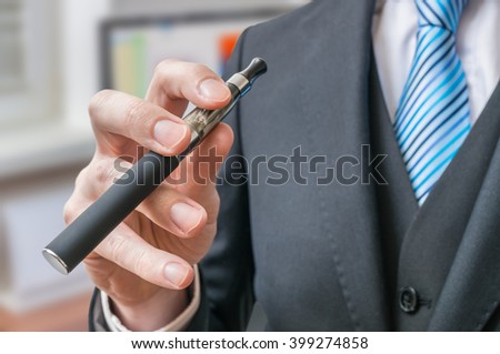 Businessman holds e-xigarette or vaporizer in hand.