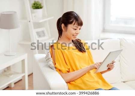 people, technology and leisure concept - happy young asian woman sitting on sofa with tablet pc computer at home