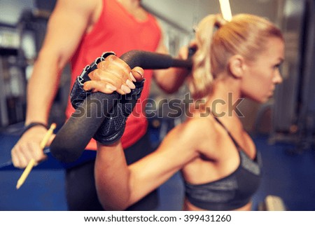 sport, fitness, teamwork and people concept - close up of young woman and personal trainer flexing muscles on cable gym machine