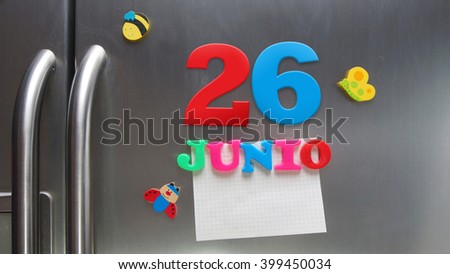 Junio 26 (June 26 in Spanish language) calendar date made with plastic magnetic letters holding a note of graph paper on door refrigerator. Spanish version
