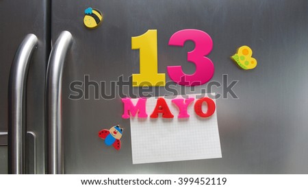 Mayo 13 (May 13 in Spanish language) calendar date made with plastic magnetic letters holding a note of graph paper on door refrigerator. Spanish version                