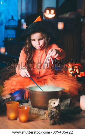 Little girl in a costume of witch making potion with magic wand; Halloween studio decoration