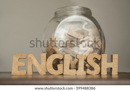 Word english made with block wooden letters next to a pile of other letters in transparent glasses jar or bank on gray background 