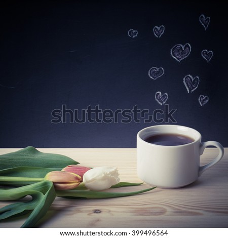 Romantic theme on a chalkboard behind a wooden table with cup of coffee and tulips. Toned.
