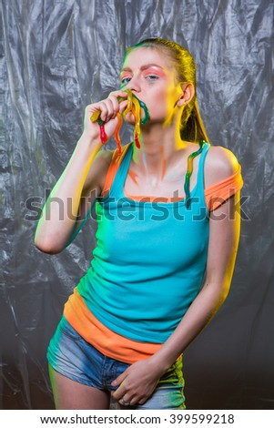 Young woman with colorful make up holds gummy jelly worms candies in mouth.