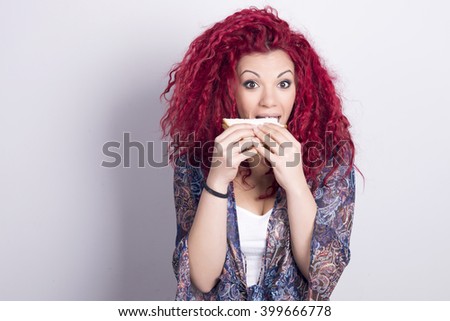 Funny and happy woman eating a sandwich. Indoors, over a grey background.