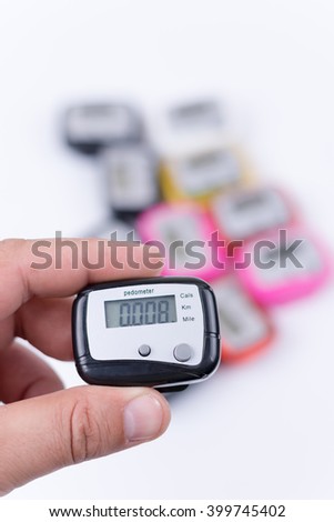 Digital pedometer in the hand over pile of pedometers.