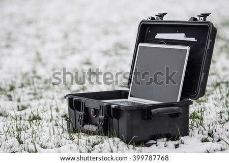 Opened plastic black protector case with laptop lying on the grass and snow