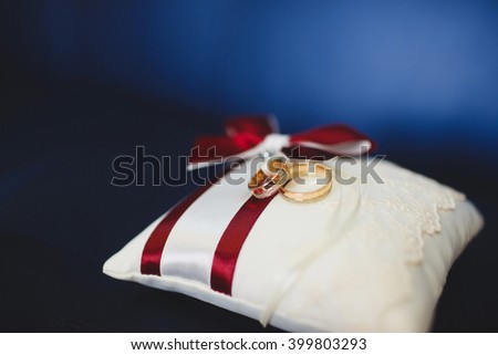 Wedding gold rings on white pillow with red ribbons