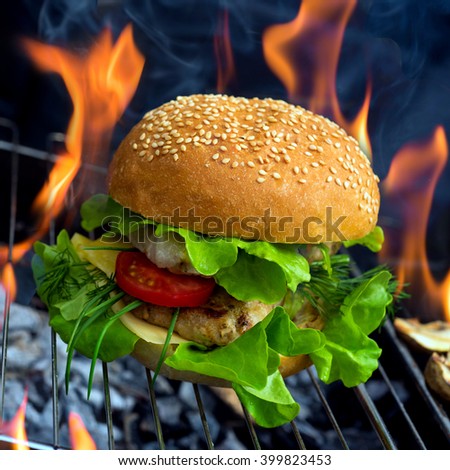 Sandwich with chicken burger, tomatoes, cheese and lettuce and flame on background