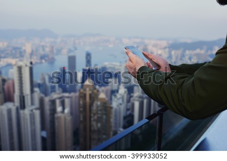 Close up business man is reading financial news in internet via cell telephone, while is standing on skyscraper building roof with view of developed China's business center background with copy space