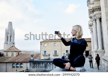 Woman traveler is making photo with mobile phone camera of a old tower,while she is relaxing in the fresh air after excursion in museum. Female tourist is shooting video of city view on cell telephone