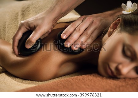 Massage with hot basalt stones. Beautiful deep charming light. Royalty-Free Stock Photo #399976321