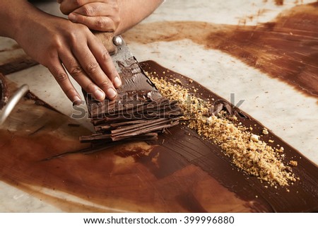 Close up professional black man chief hands cook circles from melted homemade chocolate on stone marble table in bakery