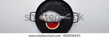 Close up presentation of fresh wild sea bream on grill pan, with grapefruit slice below, ready to cook, isolated in center of white table with spaces for your text on sides