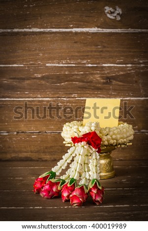 Thai flower garland , red rose, Gardenia and Crown Flower,Blank Yellow paper, posted ,post-it ,note ,Sticky Note  on Wood Table Background, Rustic Still Life Style