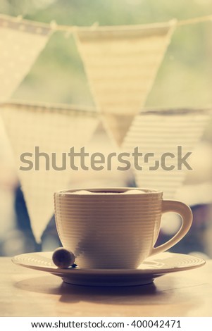 A cup of coffee and spoon on wooden table with fabric flags background, vintage tone color.