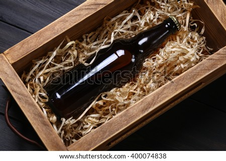 Bottle of beer in a wooden crate with wood shavings on a dark wooden surface Royalty-Free Stock Photo #400074838