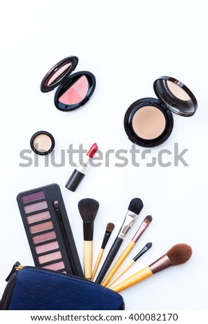 Flat lay photo of makeup bag with various brush and cosmetics on white background, top view 