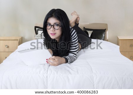 Pretty woman using a tablet computer while lying on her bed and looking at the camera