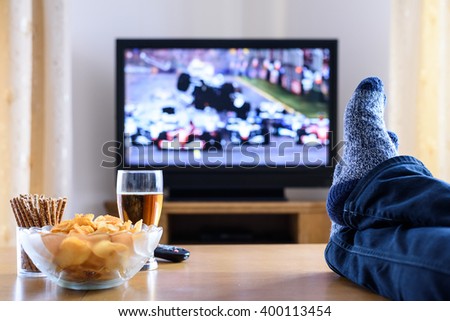 Television, TV watching (formula one race) in living room with feet on table - stock photo
