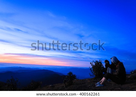 A group of people sitting on the mountains watching sun at sunrise.