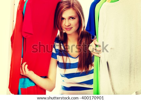 Happy teenage woman between clothes on hanger