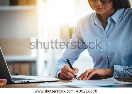 Signing new contracts. Close-up part of young woman signing documents while sitting at her working place 