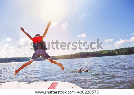 Kids jumping off a boat into the lake. Focus on boys legs and boat, lens flares from sun. Royalty-Free Stock Photo #400220575