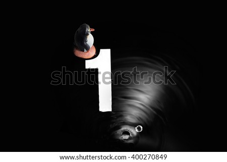 A  penguin(miniature) with blurry water wave and reflection of number.Number 1
background.