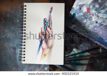 Sketchbook painting of artist's colored with paint hand holding a brush 